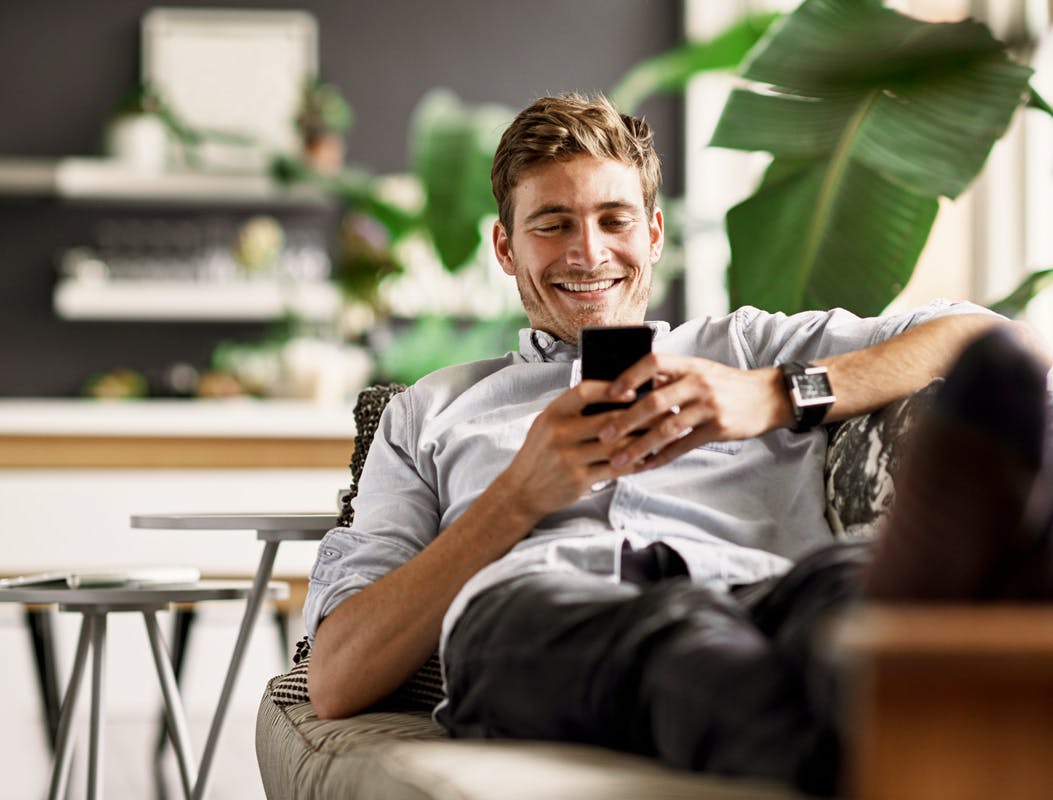 Personne souriante assise sur un canapé regardant un smartphone dans une pièce moderne.